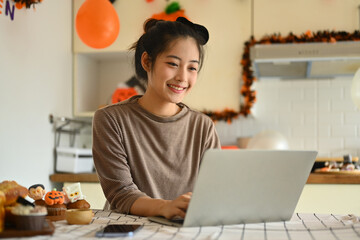 Happy young woman using laptop in a kitchen decorated for Halloween