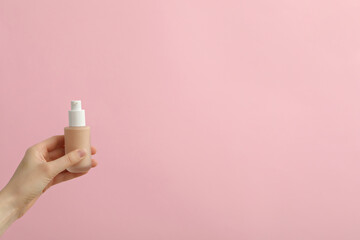 Bottle with foundation in female hand on pink background, space for text