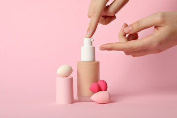 Foundation, cosmetic sponges and female hands on pink background