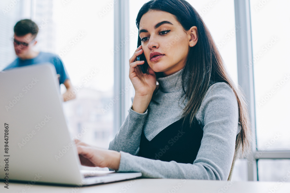Aufkleber serious businesswoman calling on smartphone while checking email on laptop computer using wireless i