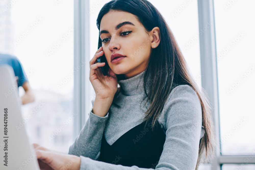 Aufkleber serious businesswoman calling on smartphone while checking email on laptop computer using wireless i