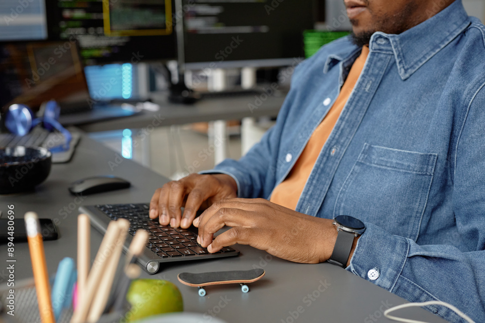 Poster cropped shot of male african american software developer writing code working at desk with multiple 