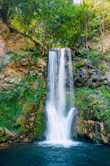 Veliki Buk waterfall in Serbia flows gracefully through a lush green forest, its cascading waters blending harmoniously with the natural beauty of the landscape.