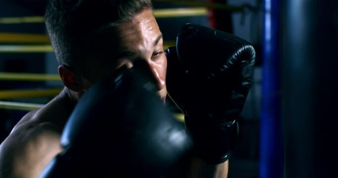 Super slow motion close up of determined sporty male athlete with gloves is fisting punching bag during boxing workout training to achieve victory on competition at boxing ring at 1000 fps.