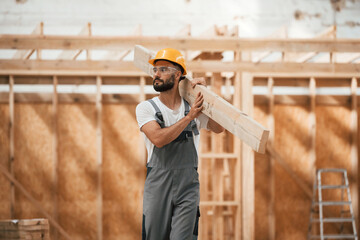 Walking, holding plank. Industrial worker in wooden warehouse