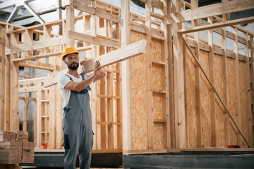Fototapeta premium Carrying the plank. Industrial worker in wooden warehouse