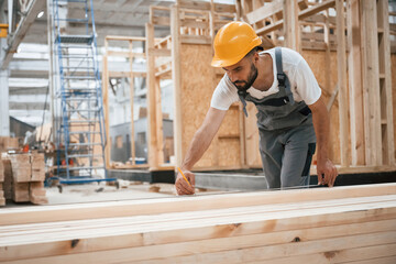 Standing, marking plank by pencil. Industrial worker in wooden warehouse