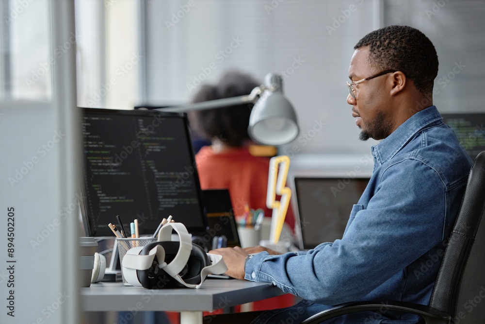 Poster side view of male african american software developer working on computer writing code for vr app wh