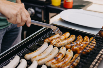 Close-up of a hand using tongs to flip sausages on a charcoal grill