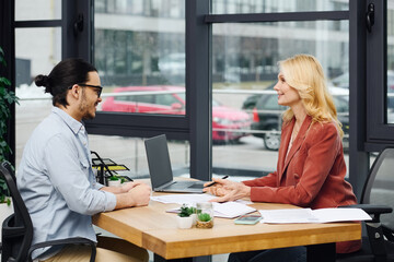 Man and woman engaging in discussion at a desk in an office setting.