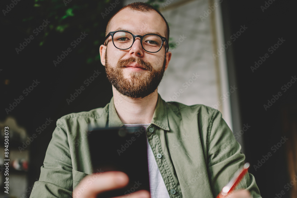 Poster below portrait of bearded hipster student in stylish eyeglasses for vision correction holding modern