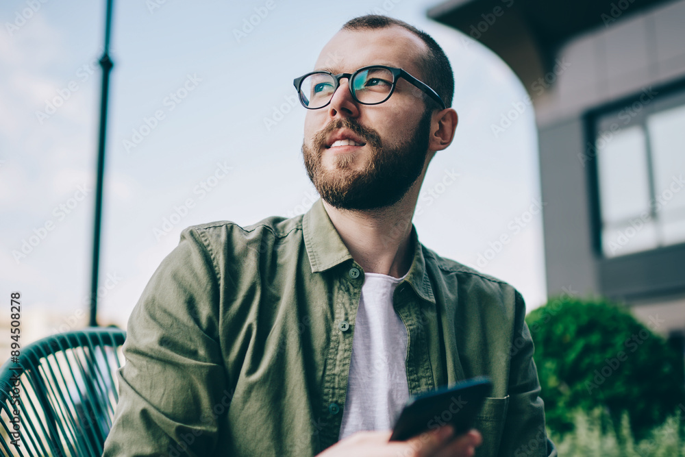 Poster pondering bearded young man looking away while thinking on idea for publication in blog on smartphon