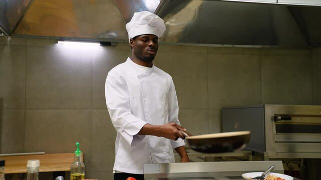 African American chef in restaurant making flambe on frying pan