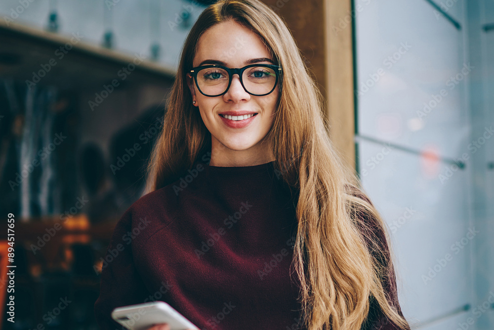 Poster caucasian female student sitting with smartphone and holding open text book in hand while looking to