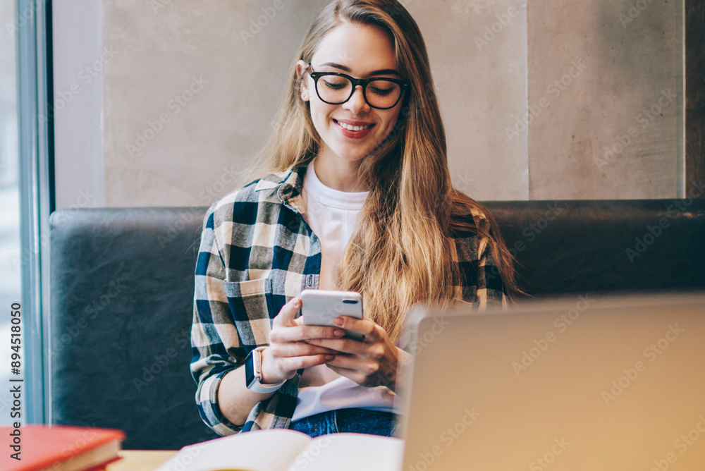 Poster smiling hipster girl messaging with friends via cellular phone after working on modern laptop comput