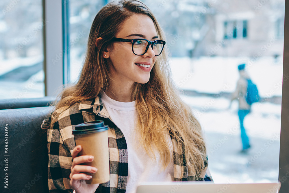 Poster happy female programmer looking at cafeteria window with cute smile on face while enjoying cup of co