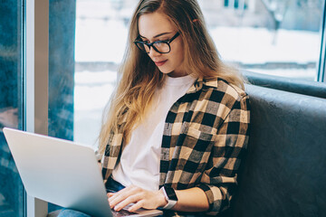 Beautiful concentrated female copywriter creating new article for website via digital computer...