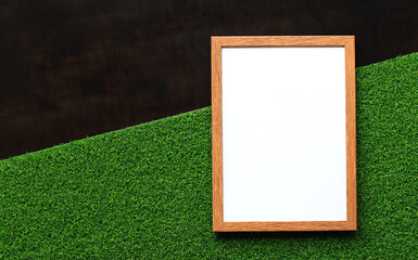 Blank frame with white sheet on dark wooden background with green artificial grass. Blank photo with copy space