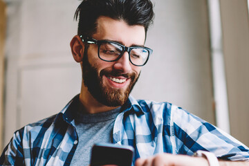 Smiling successful hipster guy in eyewear checking time on wearable smartwatch while waiting for...