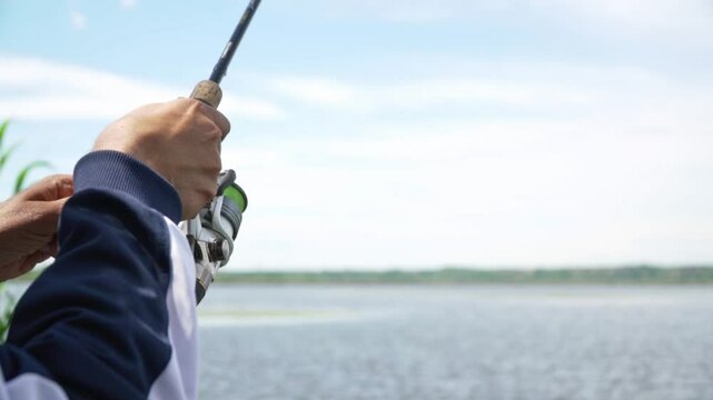 Close up of man spinning a reed to catch a fish from a blue lake