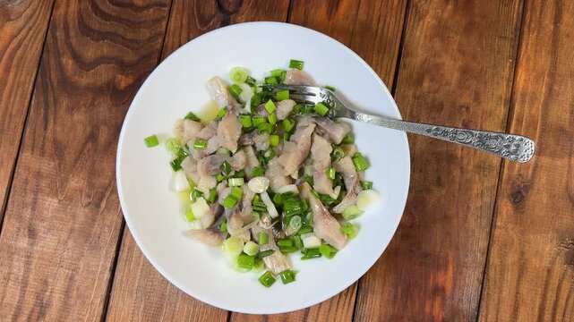 Sliced pickled herring with green onion on dish with fork
