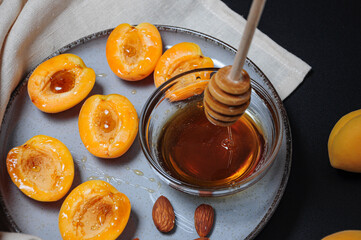 Apricots on plate with bowl of honey pouring from honey spoon