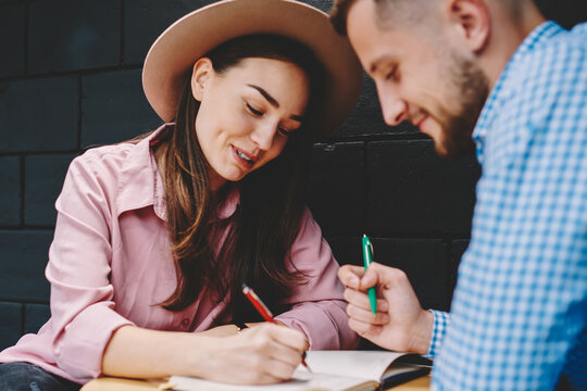 Couple in love dressed in casual wear discussing plan of common rest and writing down checklist in notepad spending leisure time in modern coffee shop.Young marriage noting list to do in notebook