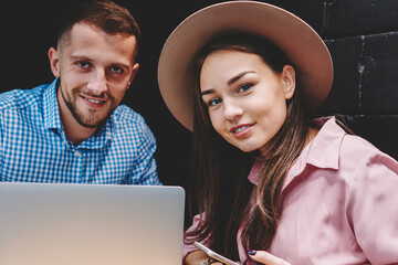 Portrait of happy couple in love have meeting in cafe interior and using modern smartphone and laptop computer.Positive girlfriend and boyfriend smiling at camera while working together at netbook