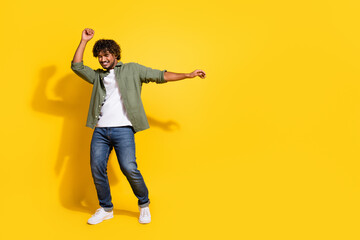 Fototapeta premium Portrait of young handsome carefree drunk student funny indian guy in khaki shirt dancing summer music vibes isolated on yellow color background