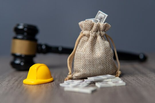 Closeup image a bag of money, hard hat and gavel on a wooden table. Workers compensation, labor law concept.