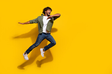 Portrait photo of young funny mexican guy in khaki shirt and jeans jumping with dab pose trend isolated on yellow color background