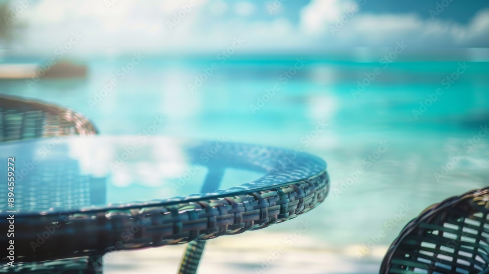 Poster a close-up view of a glass-top table with a woven base, set against a blurred backdrop of the ocean 