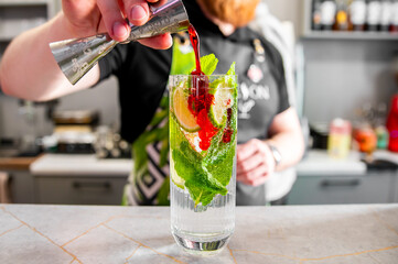 Refreshing green cocktail being poured into a glass with ice, mint, and fruit slices.