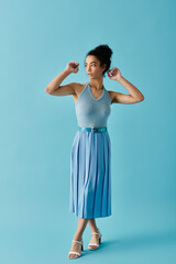 A young woman in a light  halter top and pleated skirt stands confidently against a bright blue...