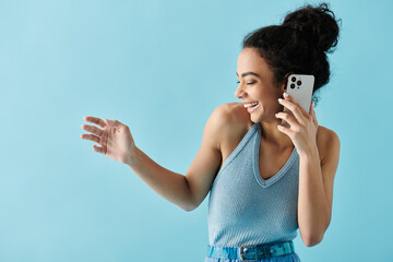 A young woman in a blue top laughs while talking on her phone against a blue background.