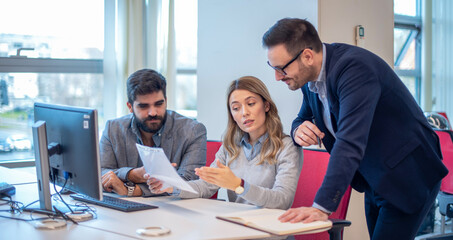 Professional colleagues working together, using computer, talking, sharing ideas and discussing new marketing plan.