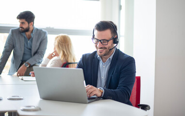 Smiling businessman wearing headset using laptop in office.