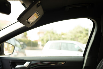 A car s sun visor is down revealing a blurry view of a car parked outside