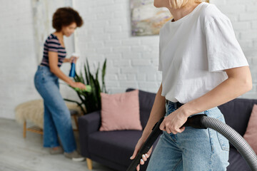 Fototapeta premium A lesbian couple cleans their modern apartment together, one vacuuming and the other wiping down surfaces.