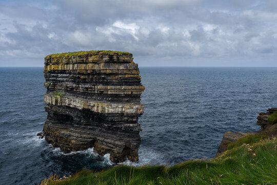 sea stack rock in the ocean near a grassy cliff