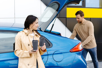 Young couple man and woman traveling by electric car having stop at charging station. Boyfriend...