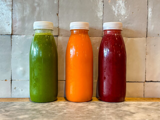 Small takeaway bottles with fresh juices or smoothies. Green juice with spinach, apple and cucumber, orange juice with carrot and orange, purple juice with beetroot. Detox days, vitamins.