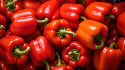 Fresh red bell peppers piled together, showcasing their vibrant color and glossy texture. The peppers have green stems and are arranged in a way that highlights their shape and freshness.