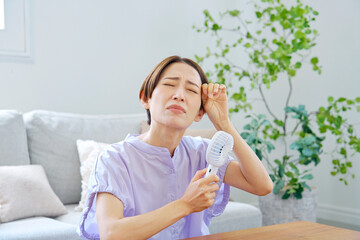 蒸し暑いリビングで携帯扇風機を使う女性