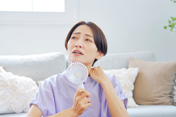 蒸し暑いリビングで携帯扇風機を使う女性