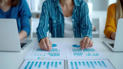 A team of professionals analyzes business charts and graphs on a desk, with two laptops open, focusing on data-driven decision-making in a modern office environment.
