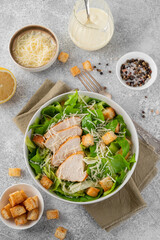 Caesar salad with lettuce, grilled chicken breast, parmesan cheese and croutons in a bowl on a gray concrete background. Copy space