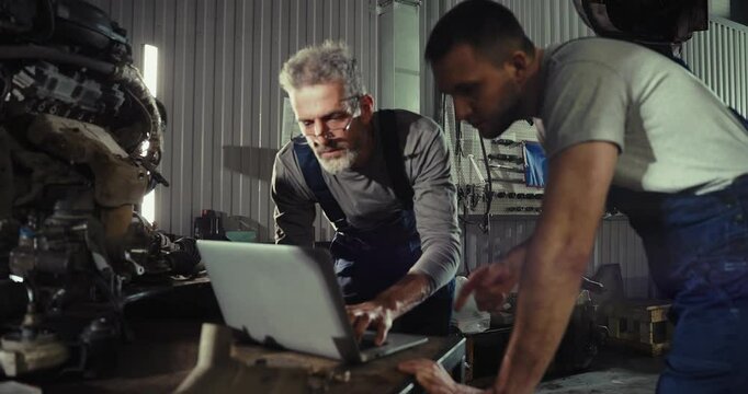 Two mechanic Caucasian man in large garage, Inspecting parts under raised car