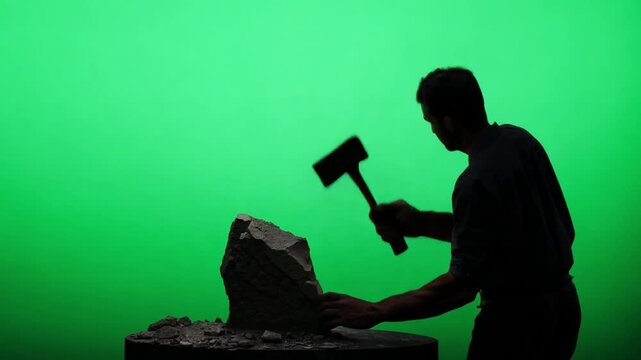 A sculptor in work clothes, chiseling stone. Green screen backdrop. High contrast lighting to emphasize details.