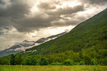 gloomy landscape with thunderclouds above the village at the foot of the mountain